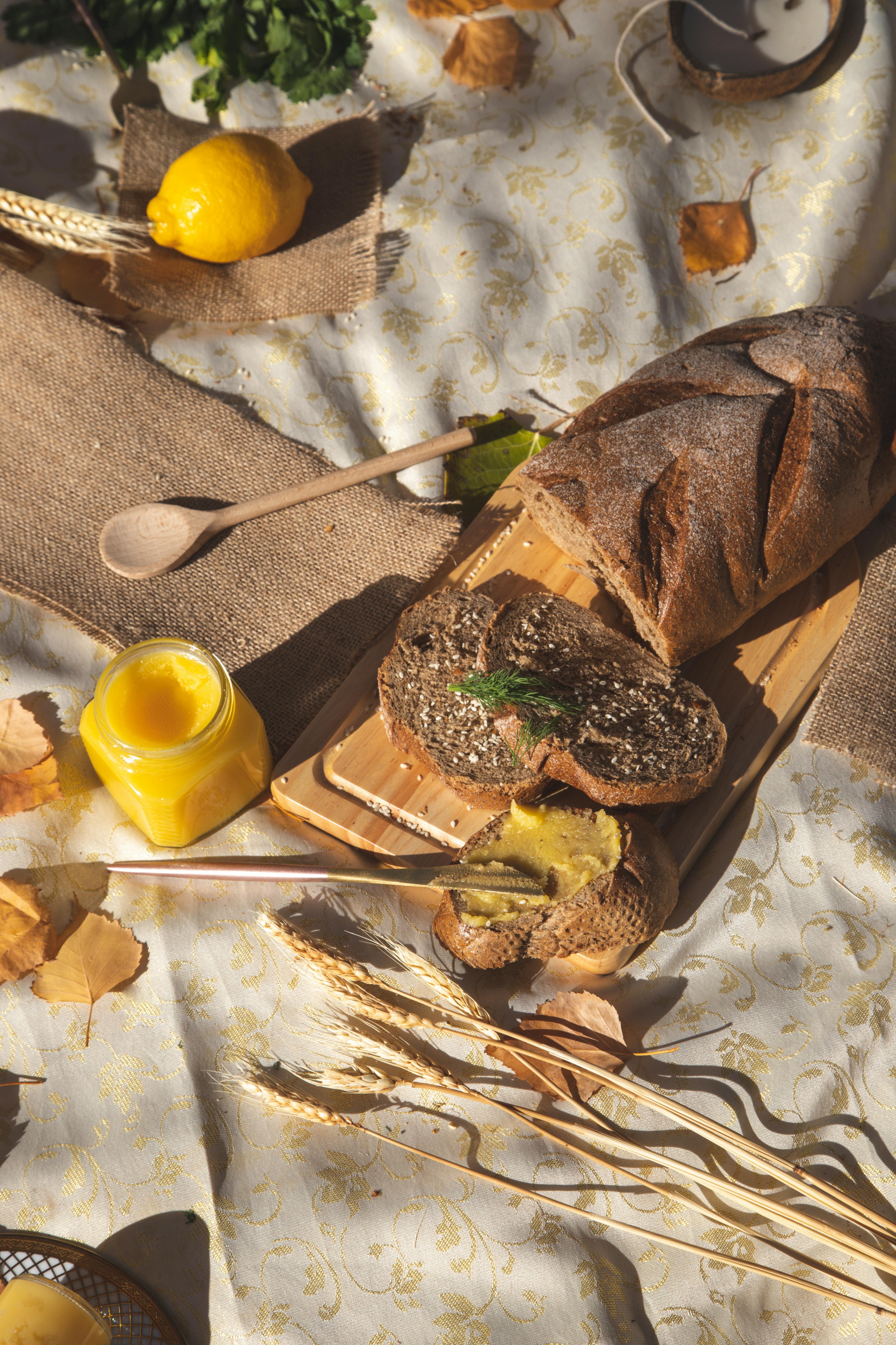 A cutting board with artisan bread on it, with various rustic elements surrounding it, such as wooden utensils, a lemon, strips of burlap fabric, and autumn leaves.