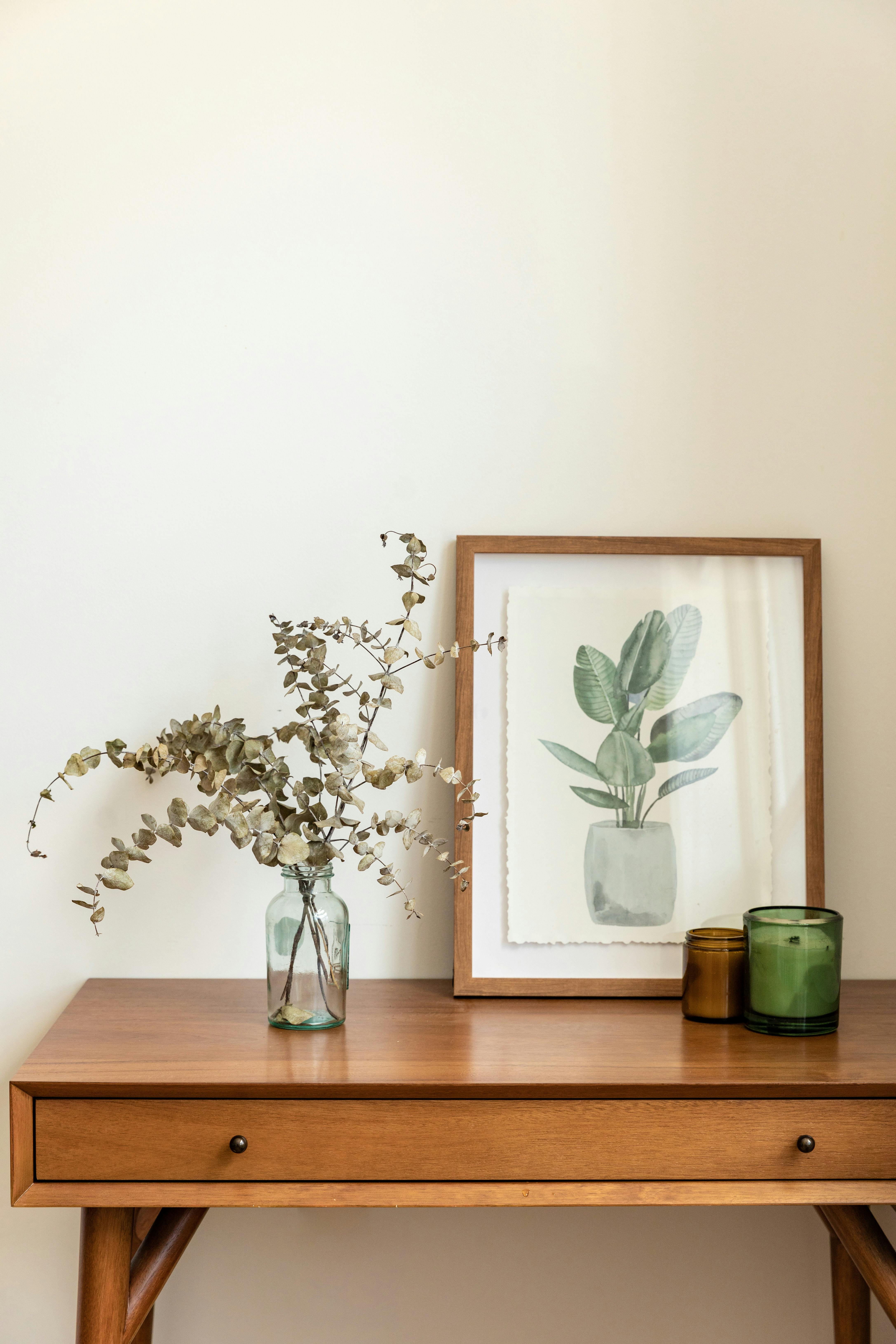 a framed botanical painting sitting in an entry table beside a vase of flowers