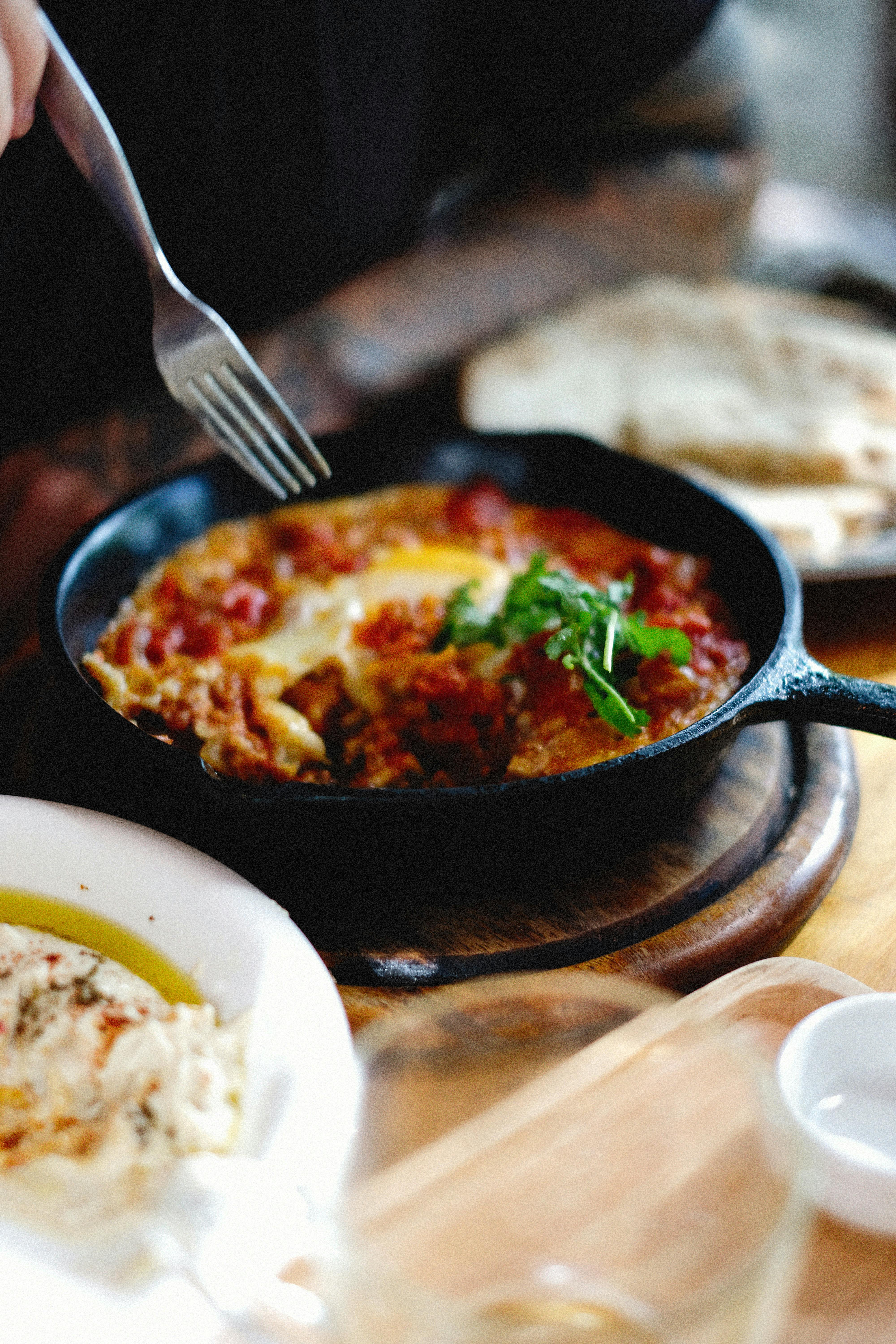 frying pan with a skillet meal in it, sitting on the table. Someone is about to poke a fork into it.